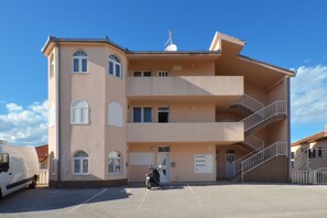 Ein mehrgeschossiges Gebäude mit einem zentralen Eingang, einem überdachten Parkbereich und einer Treppe, die zu einem Balkon führt.