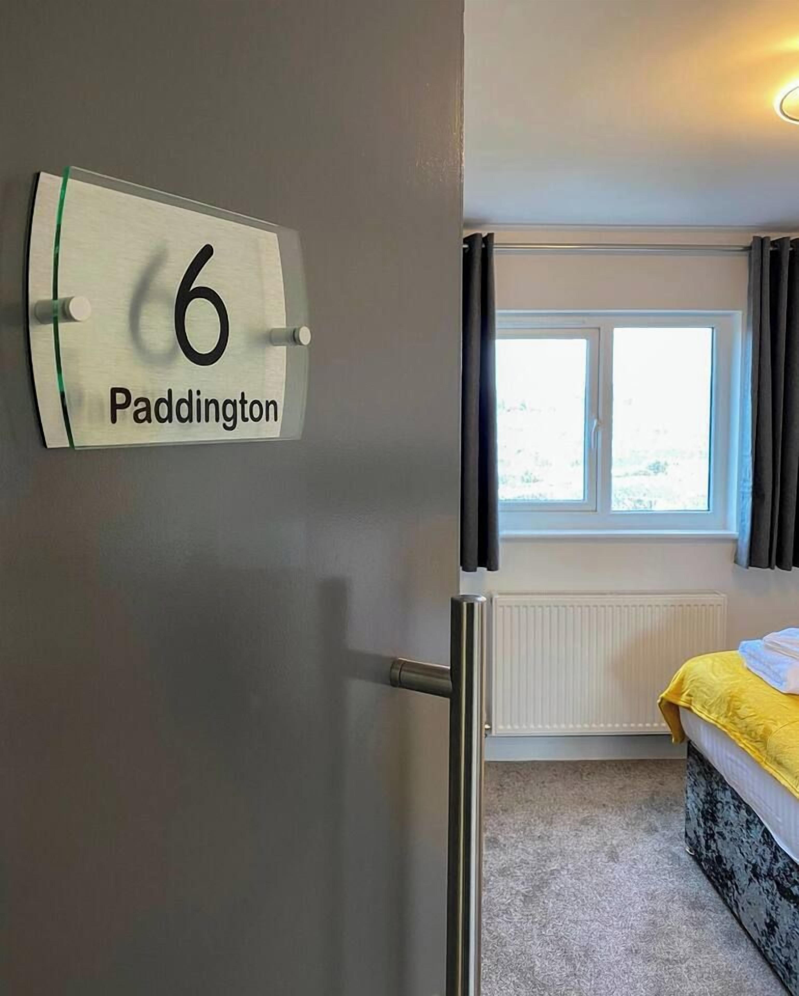 Ein Zimmer mit Bett, einem Vorhangfenster, einem Heizkörper und einer Tür mit dem Schild für Zimmer Nummer 6.