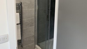 A modern bathroom with a glass shower enclosure, grey tiles, and a wooden floor. - City & Station Stays at Gulland House by Pureserviced (Plymouth)