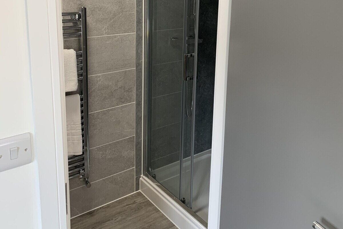 A modern bathroom with a glass shower enclosure, grey tiles, and a wooden floor.