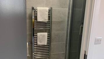 A bathroom with a glass shower enclosure, a towel rack with two towels, and a tiled wall.