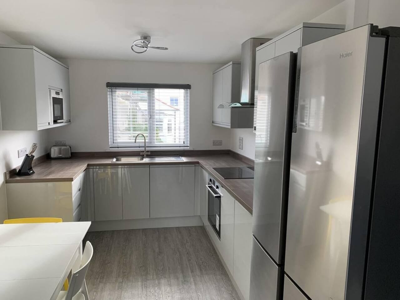 Una cocina moderna con horno empotrado, refrigerador y ventana con persianas.