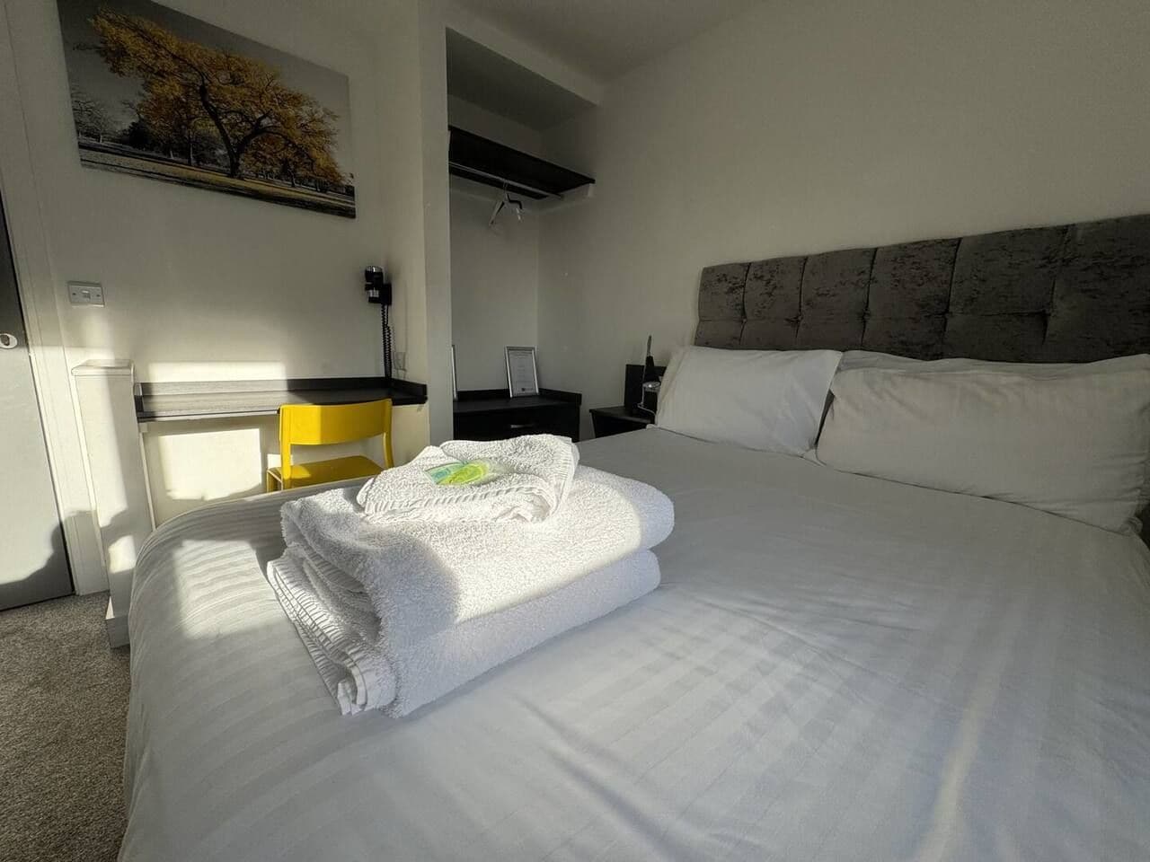 Ein Hotelzimmer mit einem ordentlich bezogenen Bett, einem Nachttisch, einem Stuhl und einem Bild an der Wand.