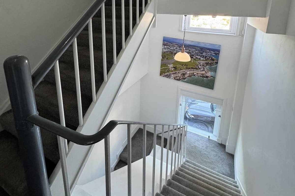A staircase with a handrail, carpeted steps, and a view of a cityscape through a window at the top.