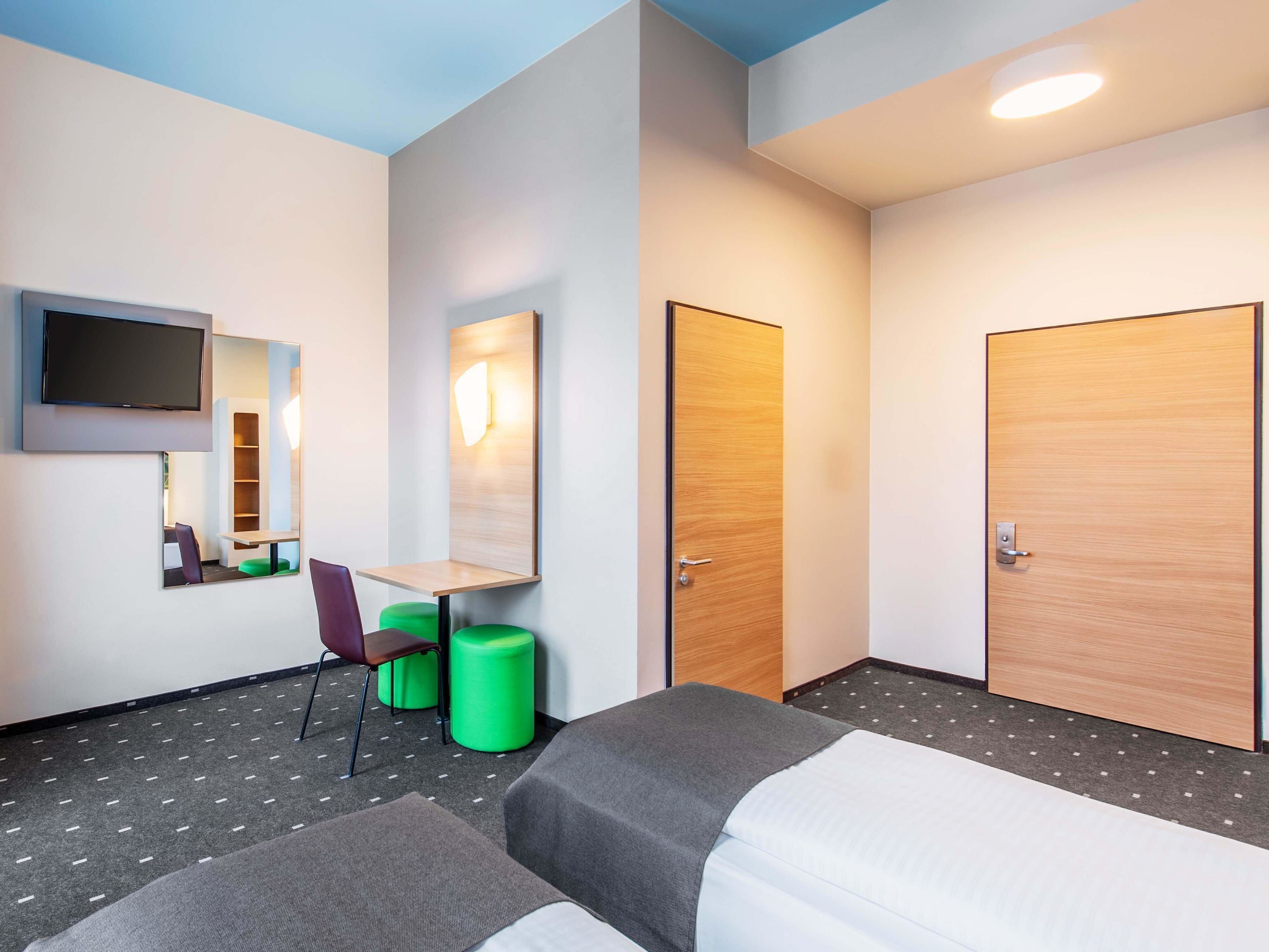 A hotel room with two beds, a desk, a chair, a TV, and a mirror.
