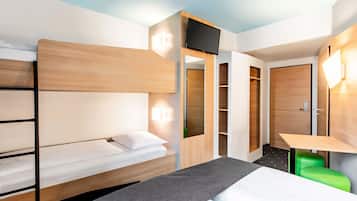 A hotel room with a bunk bed, a desk with a chair, a TV mounted on the wall, and a wardrobe with shelves.