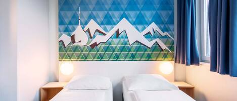 Quarto de hotel com duas camas de solteiro, um mural geométrico na parede e uma janela com cortinas.