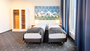 Une chambre d’hôtel avec deux lits, un tableau représentant des montagnes, une armoire et une fenêtre avec des rideaux.
