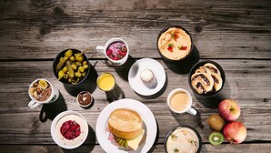 Variedad de alimentos para el desayuno, incluyendo panqueques, un sándwich y frutas frescas como manzanas y kiwi, sobre una mesa de madera.
