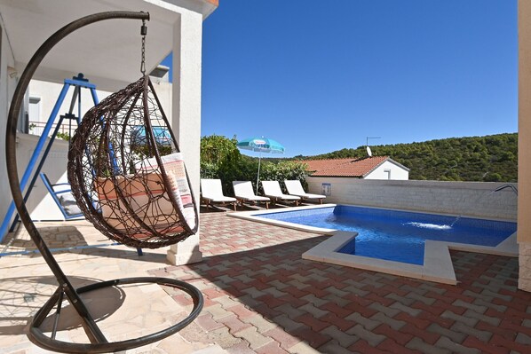 A pool area with a hanging chair, lounge chairs, and a view of a hillside.