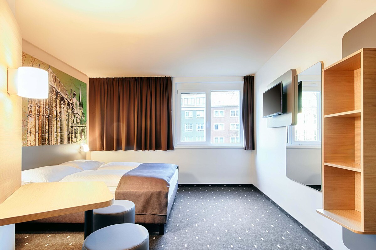 Een hotelkamer met een bed, een bureau, een stoel, een televisie en een raam met gordijnen.