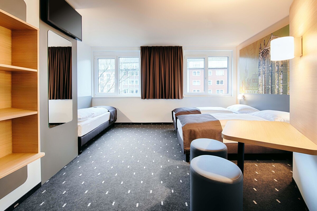 Een hotelkamer met twee bedden, een bureau, een spiegel en een raam met gordijnen.