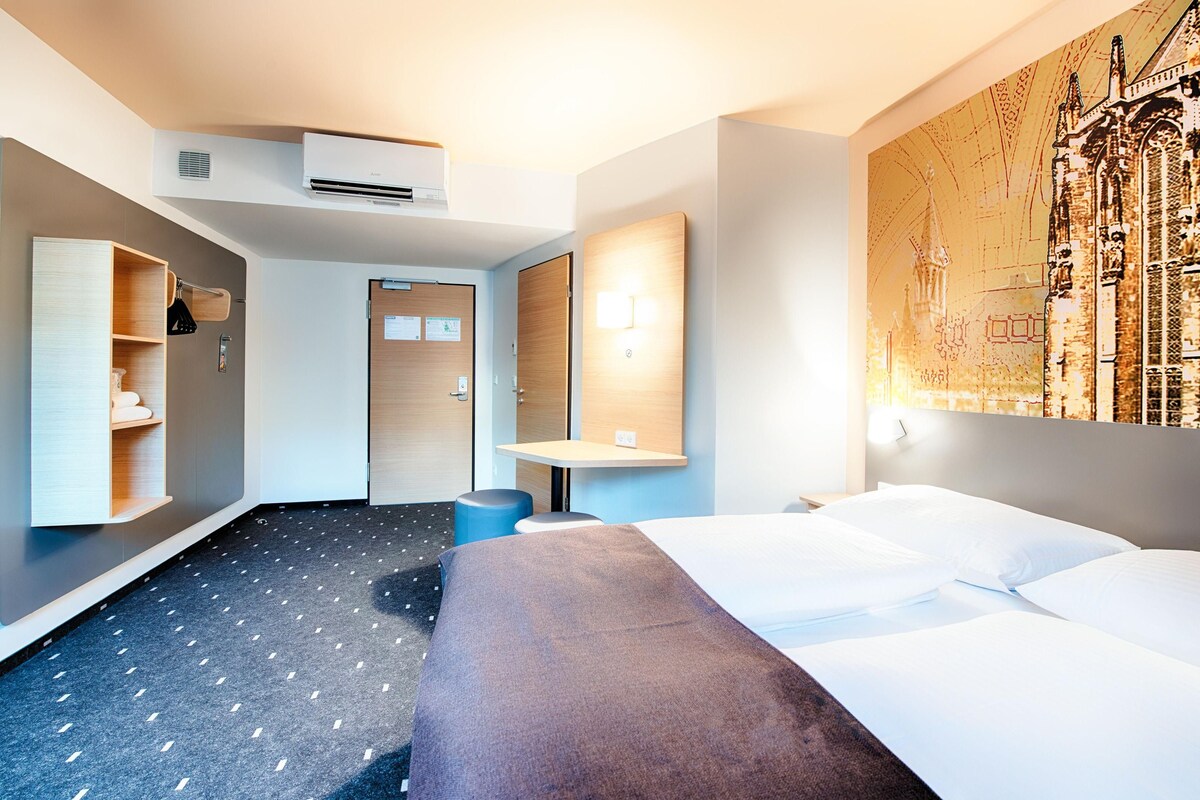 Une chambre d’hôtel moderne équipée d’un grand lit, d’un bureau, d’une armoire et d’un climatiseur fixé au mur.