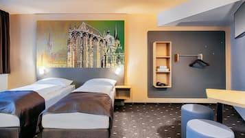 Une chambre d’hôtel avec deux lits simples, une armoire fixée au mur, une petite table et un grand tableau représentant un paysage urbain.