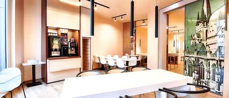 Un área de comedor moderna con una larga mesa blanca, sillas negras y una máquina de café.