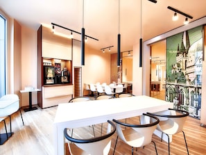 Un área de comedor moderna con una larga mesa blanca, sillas negras y una máquina de café.