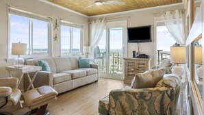 A spacious living room with a wooden ceiling, large windows, a flat-screen TV, and a view of the ocean. - LABOR DAY 2 NGT MINIMUM  SPECIAL! GORGEOUS CONDO WITH BEAUTIFUL OCEAN VIEWS! (Atlantic Beach)