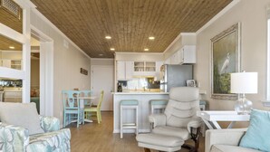 A spacious living room with a high ceiling, a dining area with a wooden table and chairs, and a kitchen with white cabinets and a bar area. - LABOR DAY 2 NGT MINIMUM  SPECIAL! GORGEOUS CONDO WITH BEAUTIFUL OCEAN VIEWS! (Atlantic Beach)