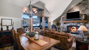 A cozy living room with a fireplace, a dining area with a wooden table and chairs, and a comfortable seating area with a leather sofa. - Beaver Creek Landing A404 3 Bedroom Condo by RedAwning (Avon)