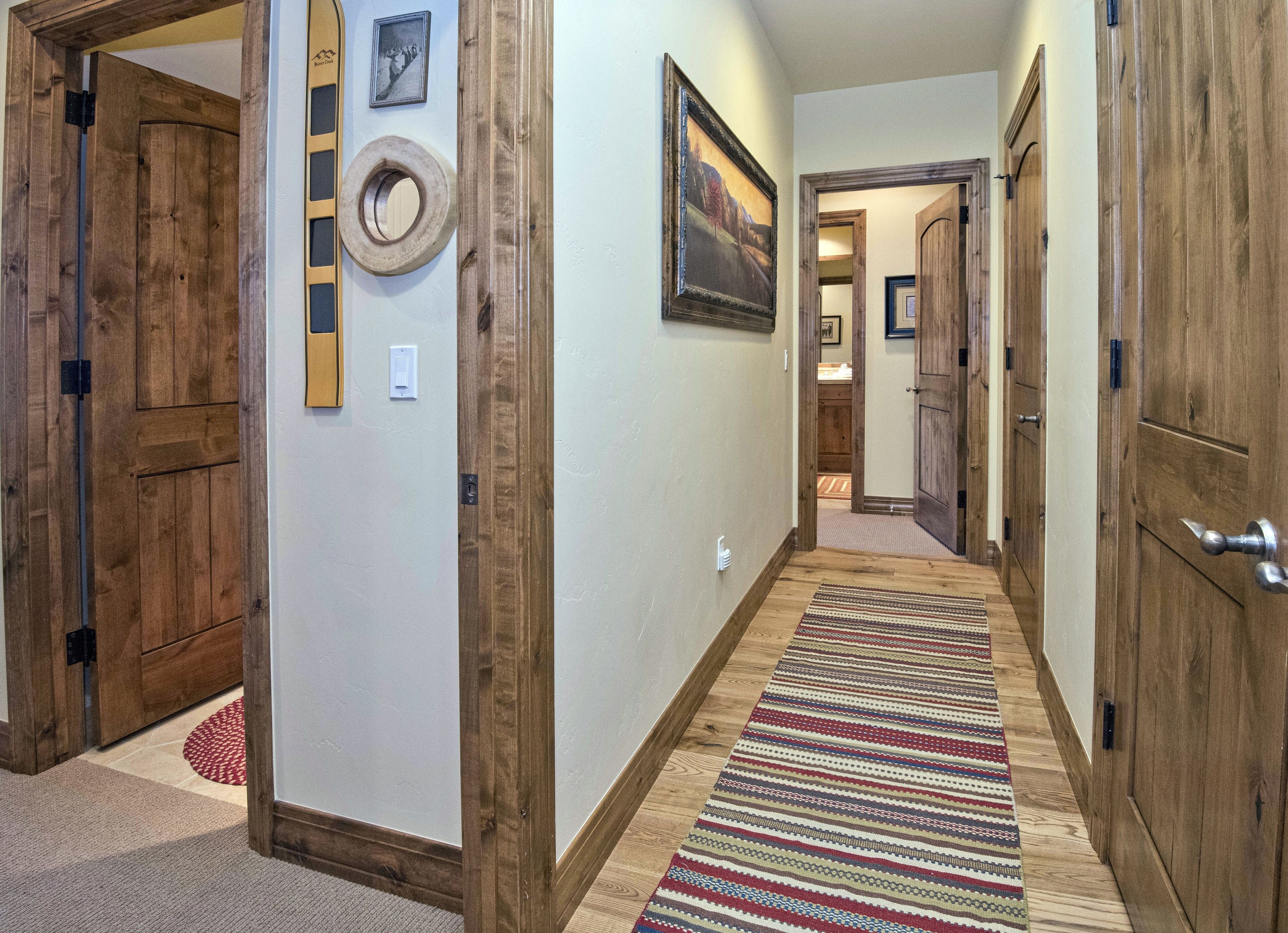 A hallway with wooden doors, a striped rug, and framed pictures on the walls.