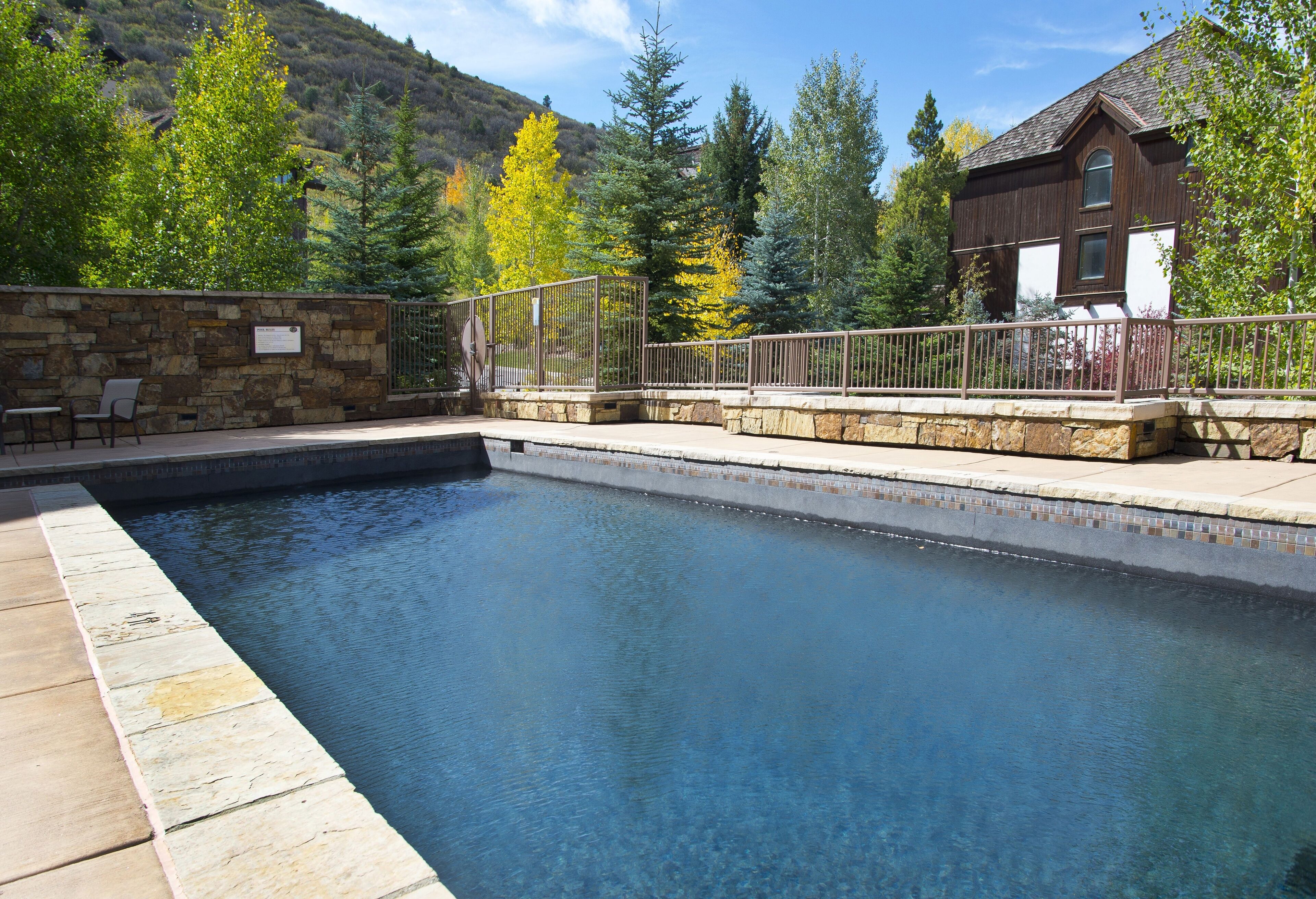 Une piscine avec des marches en pierre et un garde-corps en métal, entourée d’arbres et d’un bâtiment en bois.