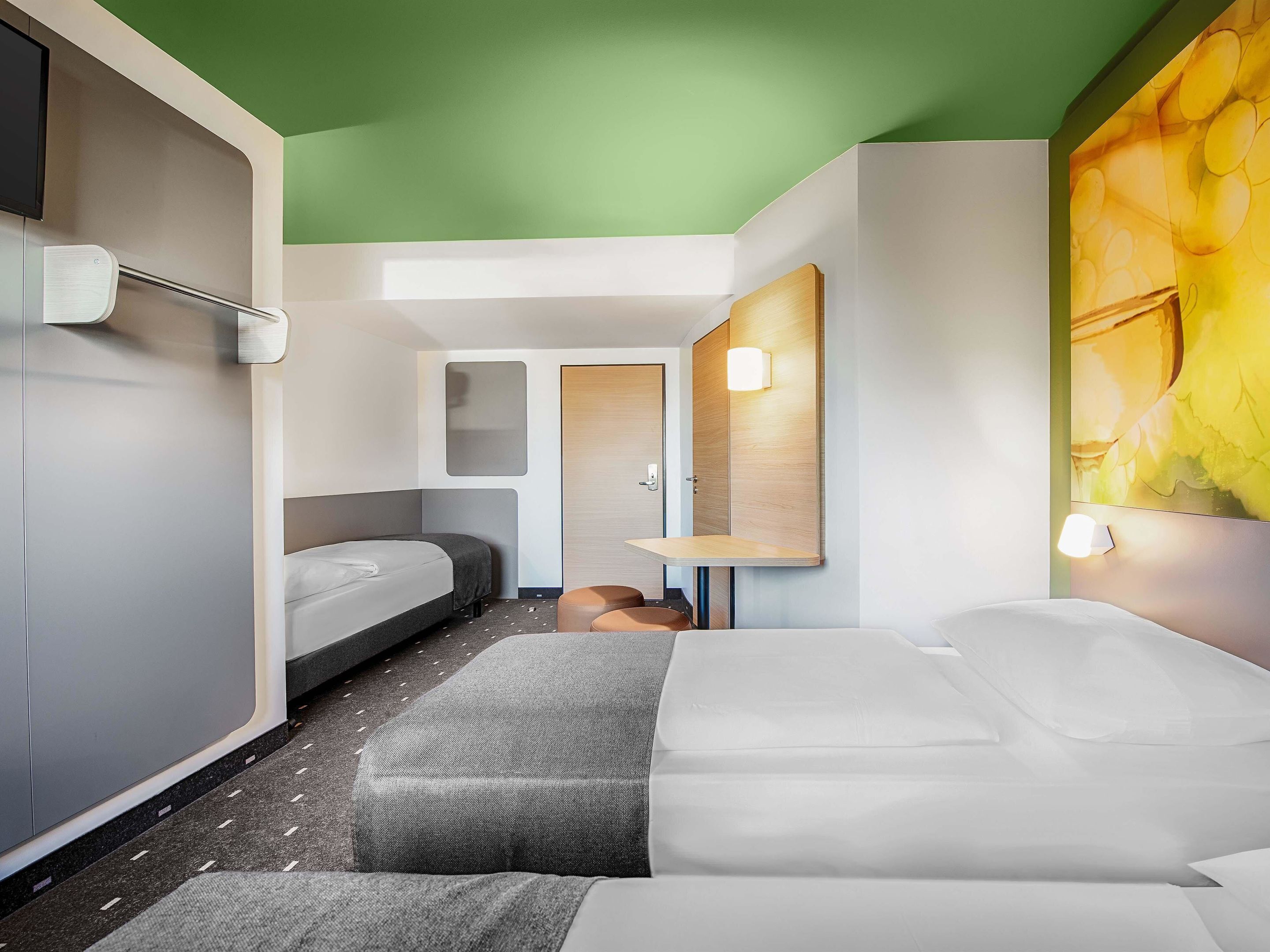 A modern hotel room with two beds, a small seating area, and a large window with a view.