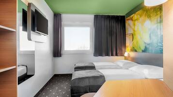 Habitación de hotel con cama, televisor montado en la pared, ventana con cortinas y un cuadro en la pared.
