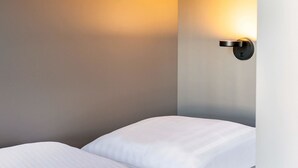 A hotel room with a bed, a wall-mounted light fixture, and a plain wall. - B&B Hotel Baden-Airpark (Rheinmunster)