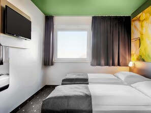 Una habitación de hotel con una cama, televisión, ventana con cortinas y un cuadro en la pared.