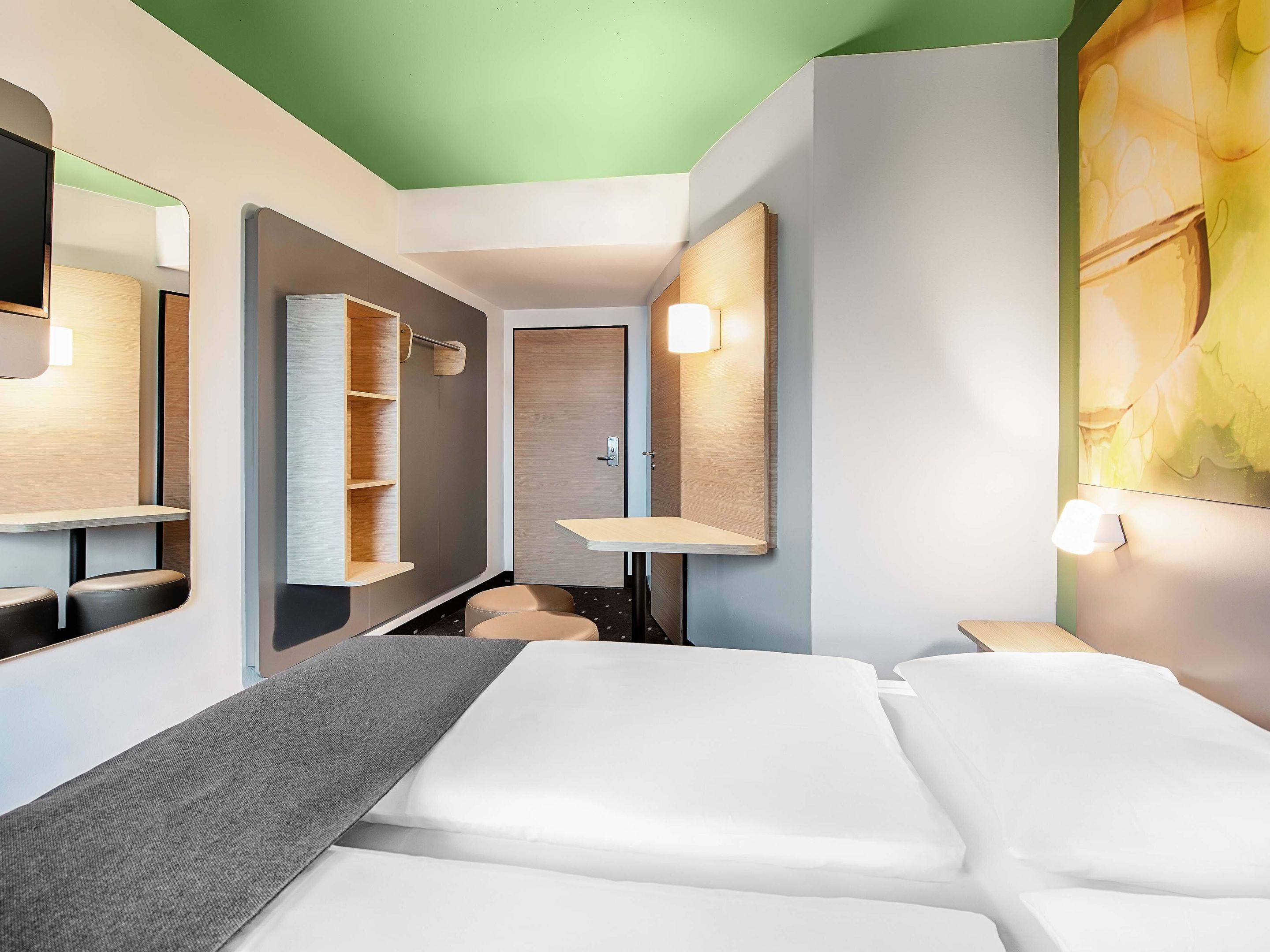 Una habitación de hotel moderna con cama, escritorio, espejo y armario.