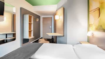 Una habitación de hotel moderna con cama, escritorio, espejo y armario.