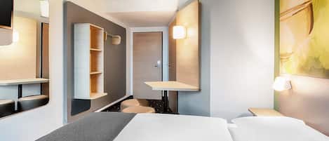 Et moderne hotelværelse med seng, skrivebord, spejl og garderobeskab.