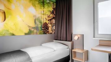 Une chambre d’hôtel moderne, équipée d’un lit, d’une petite table de chevet, d’une lampe fixée au mur et d’une fenêtre donnant sur l’extérieur.