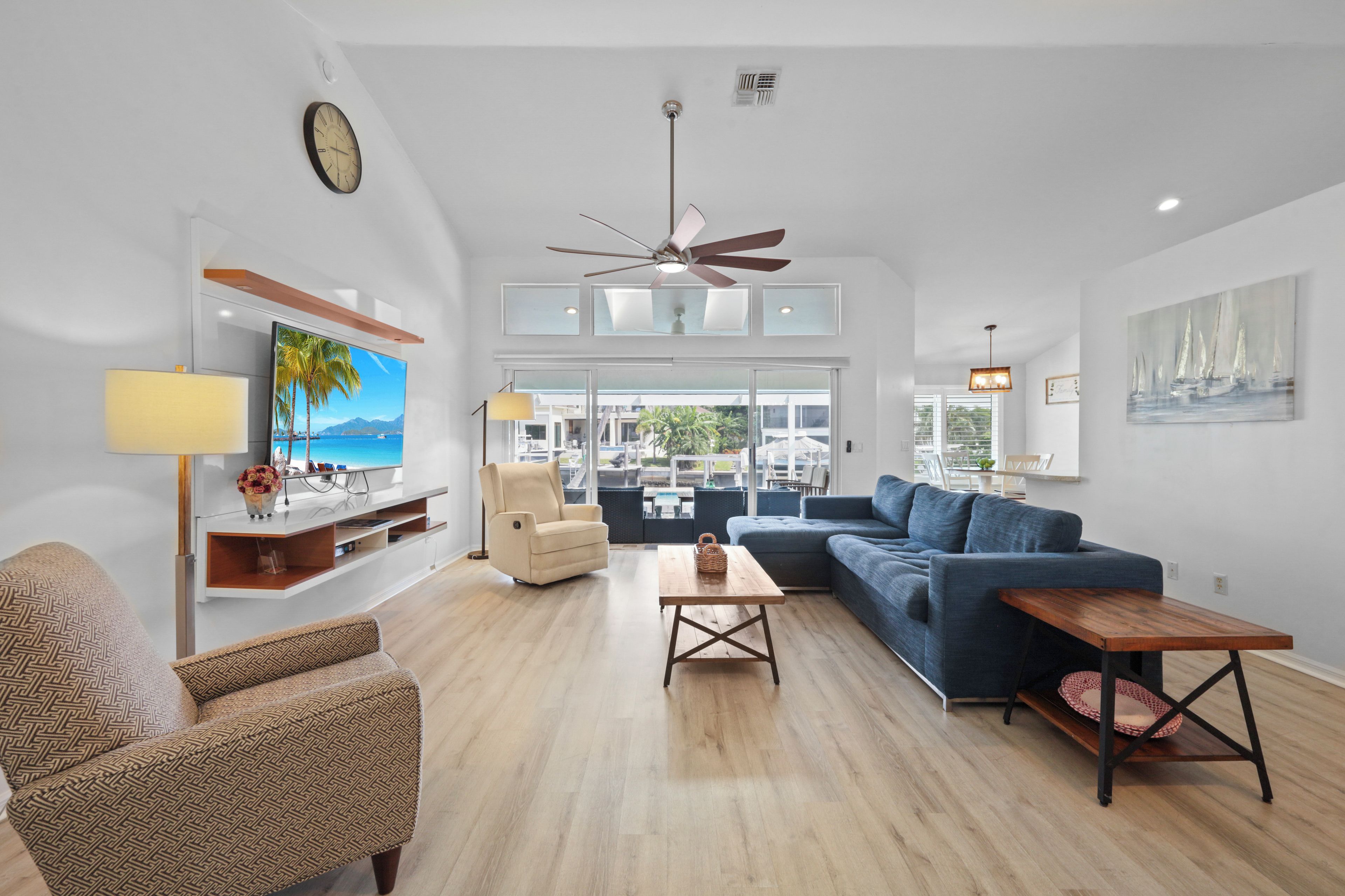 A modern living room with a sofa, armchair, TV, and ceiling fan.