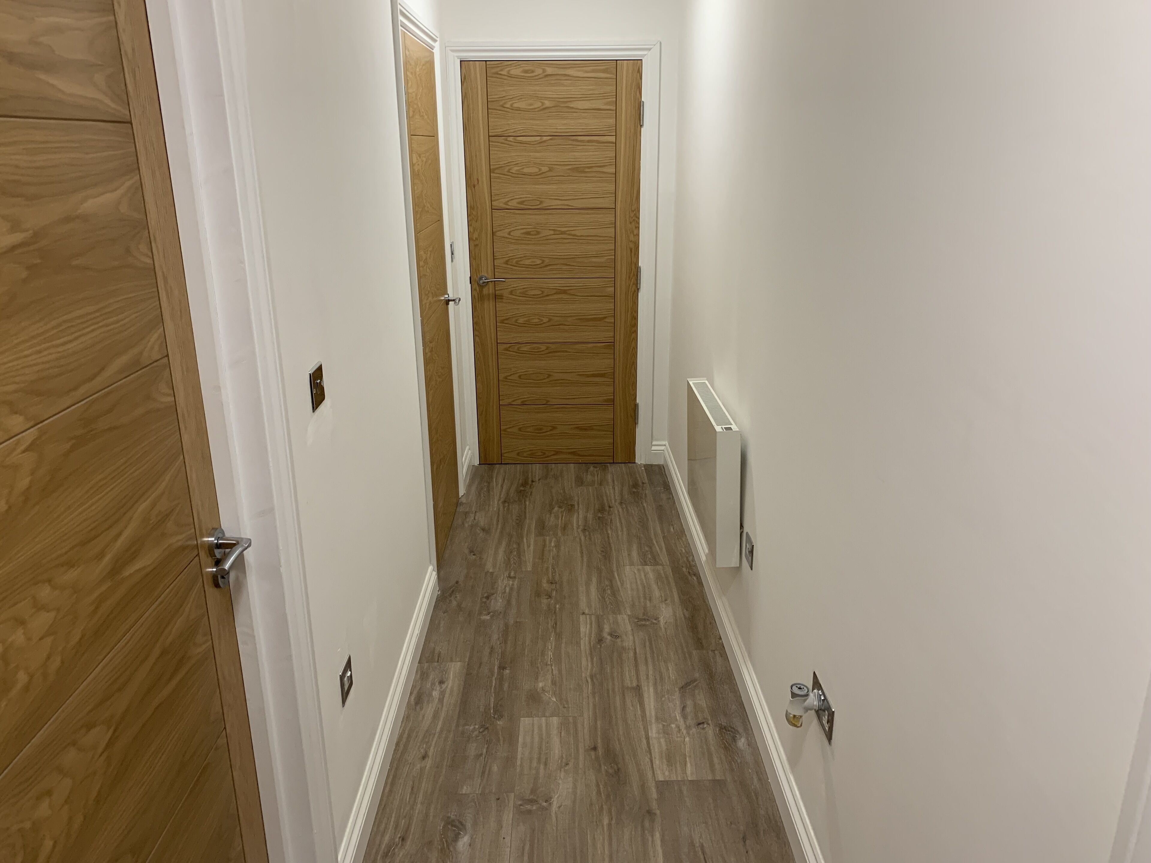 A narrow hallway with wooden flooring and white walls.