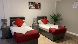 A hotel room with two beds, each with a red pillow and white bedding. There is a wall clock and a framed picture above the beds. - Impeccable 2-bed Apartment in Birmingham (Birmingham)