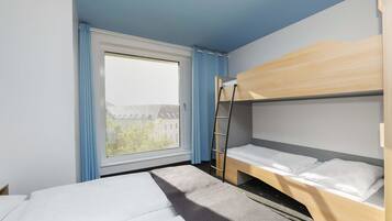 A room with a bunk bed, a window with curtains, and a view of buildings outside.