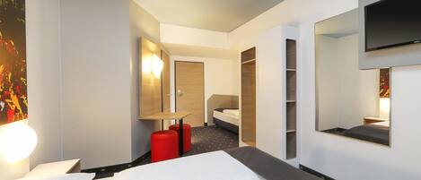 A hotel room with a bed, a desk, a chair, a wardrobe, and a TV mounted on the wall.