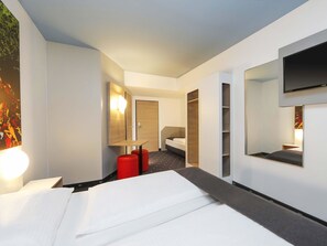 Habitación de hotel con cama, escritorio, silla, armario y televisor montado en la pared.