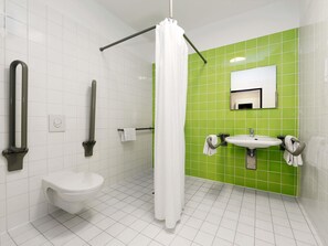 Ein Badezimmer mit weißen Fliesen, einer grünen Akzentwand, einer weißen Toilette, einem Waschbecken mit Spiegel und einer Duschkabine.