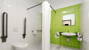Een badkamer met witte tegels, een groene accentmuur, een wit toilet, een wastafel met spiegel en een douche met gordijn.