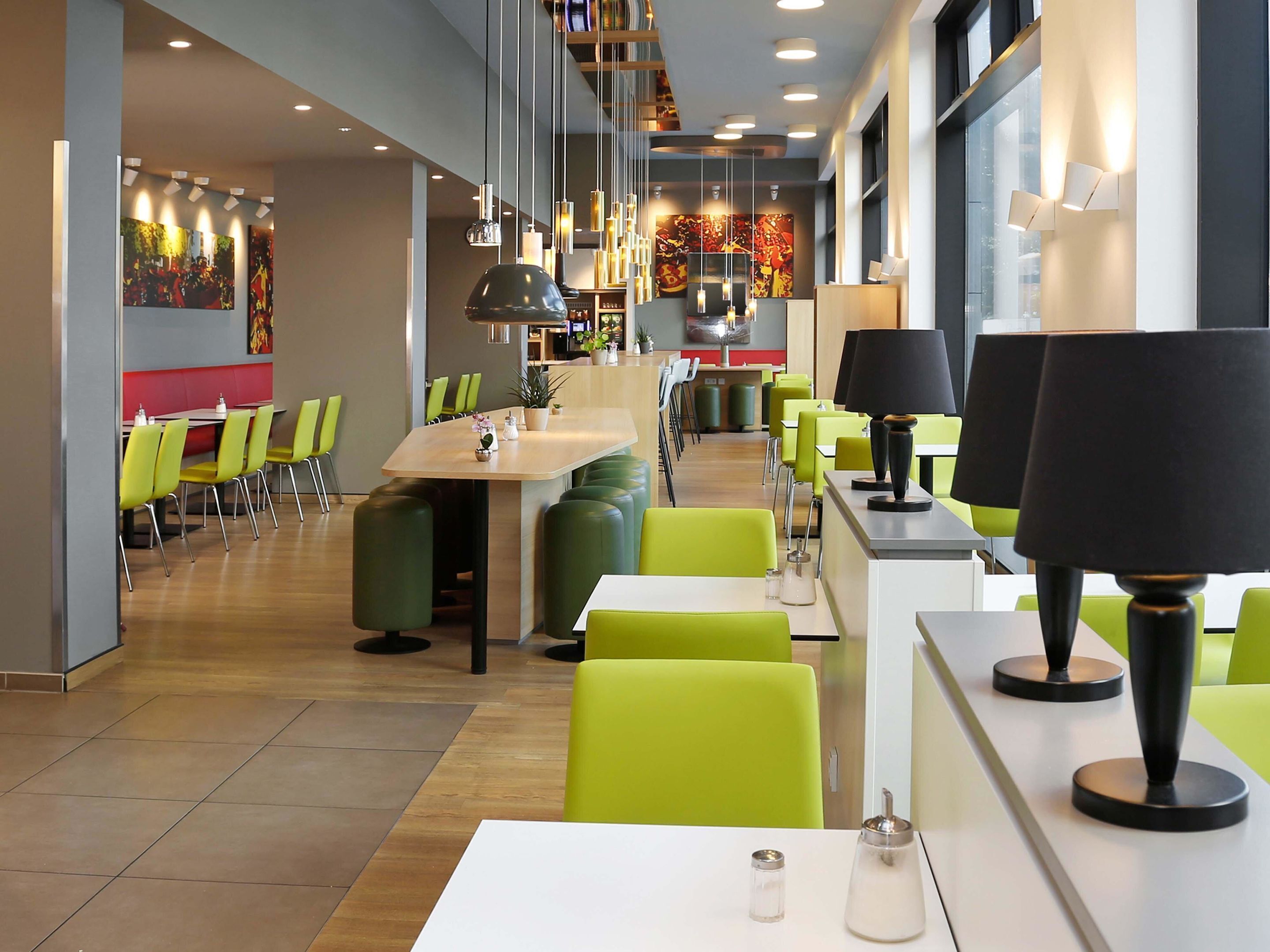 A modern restaurant with green chairs, white tables, and pendant lighting.
