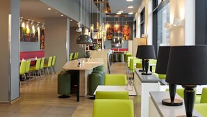 Een modern restaurant met groene stoelen, witte tafels en hanglampen.