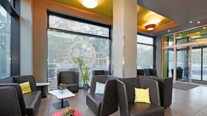 Een moderne lobby met lederen zitplaatsen, een rode accenttafel en grote ramen met uitzicht op het omliggende landschap.