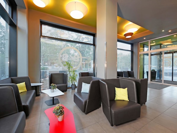 A modern lobby with leather seating, a red accent table, and large windows offering a view of the outdoors. - B&B Hotel Berlin-Tiergarten (Berlin)