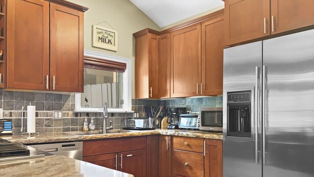 A kitchen with wooden cabinets, granite countertops, a stainless steel refrigerator, a microwave, a toaster, and a coffee maker. - Brekke's Basecamp 3 Bedroom Home by RedAwning (Park City)