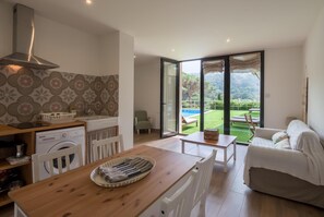 A modern kitchen with a washing machine, a dining area with a table and chairs, and a view of a pool and garden through large glass doors. - Nice apartment in small community with pool. (Begur)