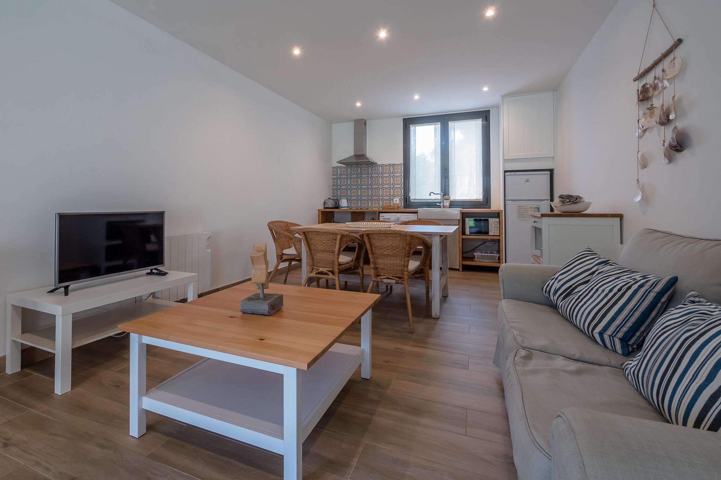 A modern living room with a TV, wooden table, and sofa. There is a dining area with chairs and a kitchen in the background.