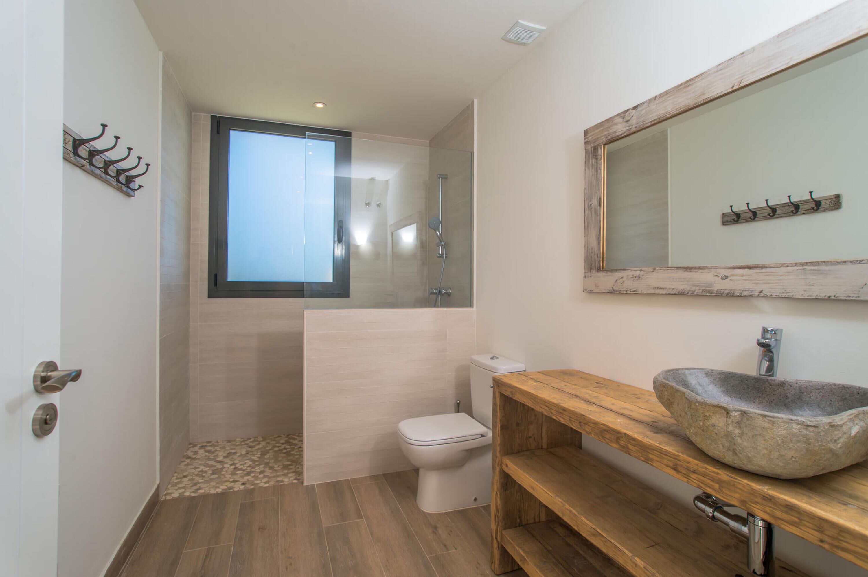 A modern bathroom with a glass shower enclosure, a wooden vanity with a stone sink, and a large mirror above the sink.