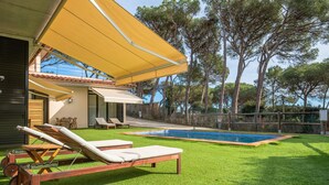 A backyard with a swimming pool, artificial grass, and lounge chairs.
